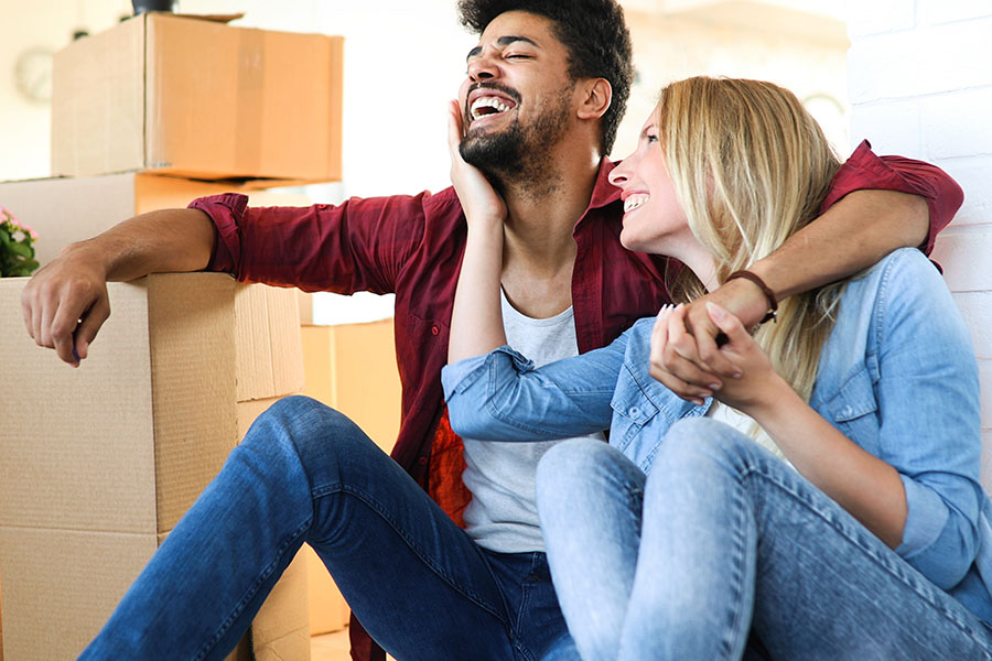 a couple sits surrounded by moving boxes in their new home.