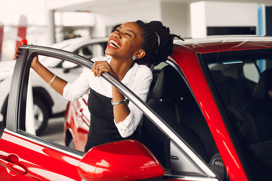  a happy woman celebrates after she buys her new red car.